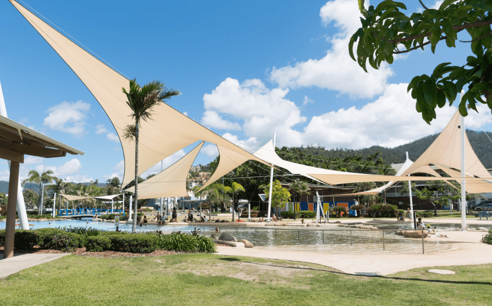 Colourful shade sail providing UV protection over a poolside lounge area